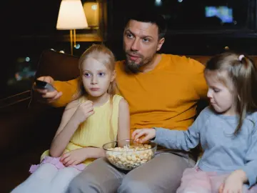 Un papá y sus hijas comen palomitas viendo una película